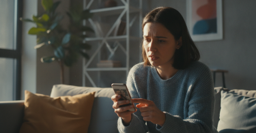 Une personne regarde son téléphone avec espoir et hésitation dans un appartement moderne.